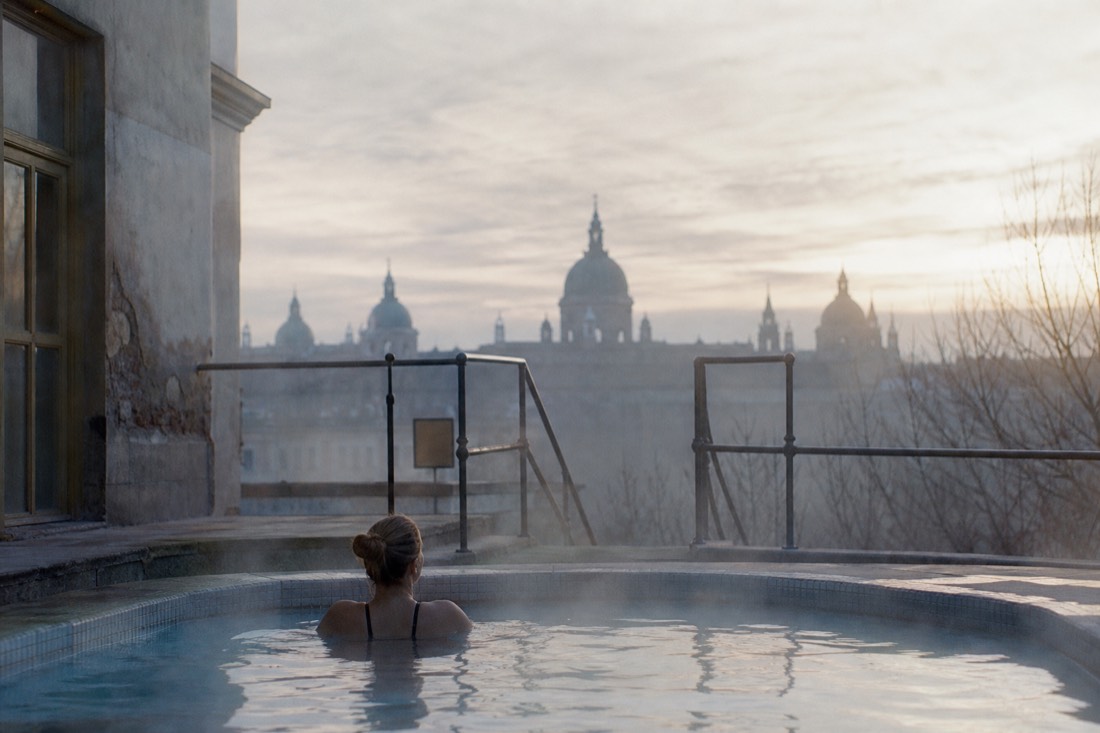Calm neighborhood thermal pool at dawn with a grand Budapest bath dome faint in the distance