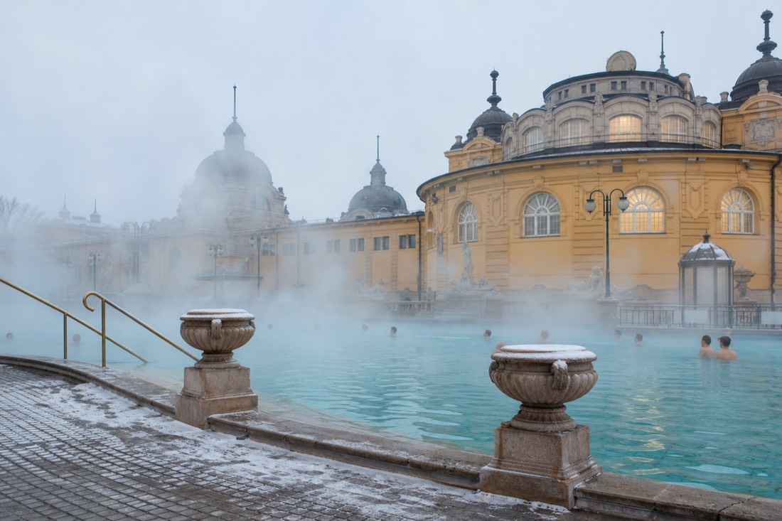 Steam pouring off a warm outdoor thermal pool at a Budapest bath palace on a cold morning, the deep well water meeting winter air