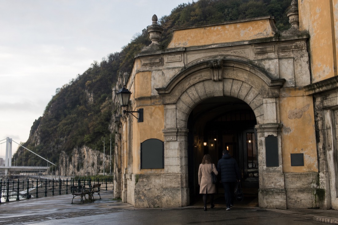 Entrance doorway of a historic Buda-side thermal bath at morning with the Danube embankment behind, no readable signage