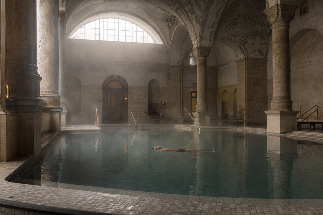 Bather floating still in a warm indoor thermal pool under an arched ceiling in Budapest